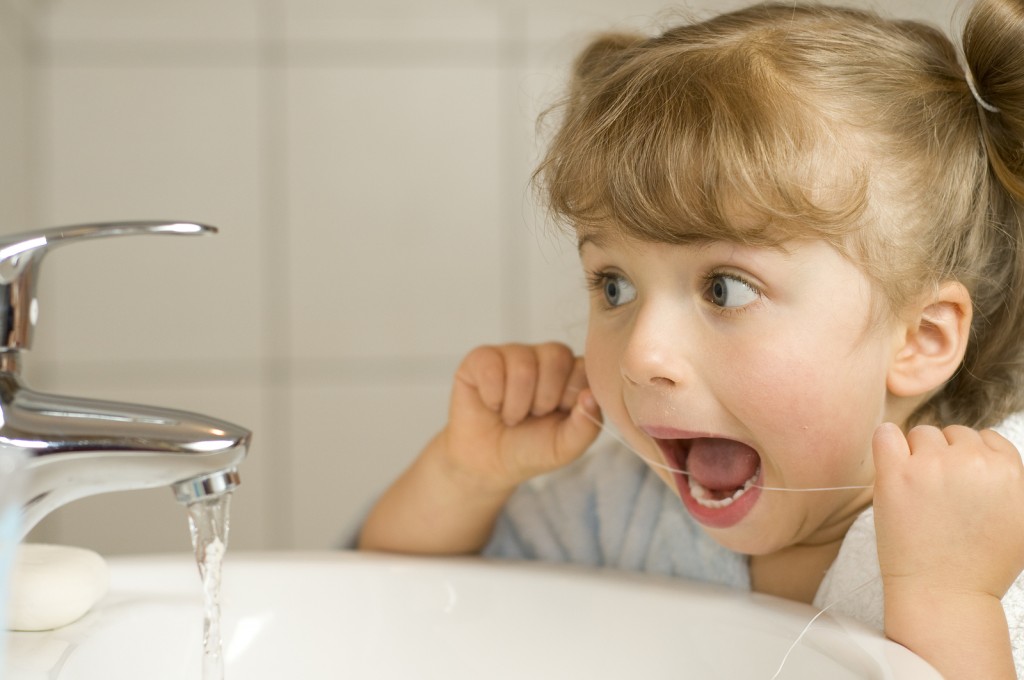 Cute girl cleaning teeth by floss in bathroom